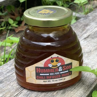 A jar of Chili Infused Honey sitting on a wooden bench.